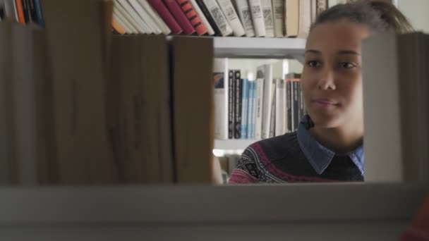 Joven estudiante afroamericana en busca de libro necesario en la estantería de la biblioteca grande tomando una apertura y satisfecho
 - Metraje, vídeo