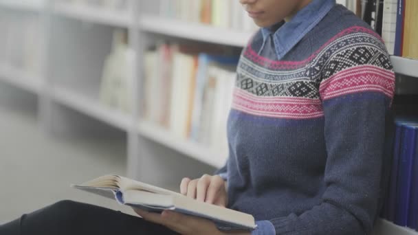 Движение Долли африканской американки читает книгу, сидя на полу в школьной библиотеке
. - Кадры, видео