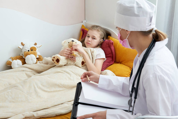 Doctor visiting sick little girl at home and writing prescription, flue concept  - Zdjęcie, obraz