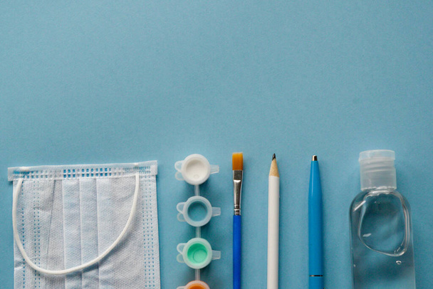 Study flatlay concept. Education supplies-pencil,pen,brush, paint, medical mask and sanitizer paint on blue background,back to school or kindergarten. summertime,creativity and learn background with - Фото, зображення