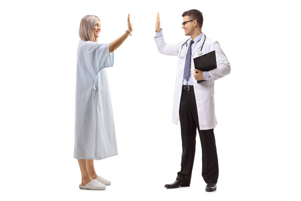 Full length profile shot of a male doctor and a woman in a patient gown gesturing high-five isolated on white background - Fotó, kép