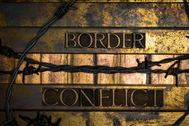 Photo of real authentic typeset letters forming Border Conflict text with barb wire on vintage textured silver grunge copper and gold background - Photo, Image