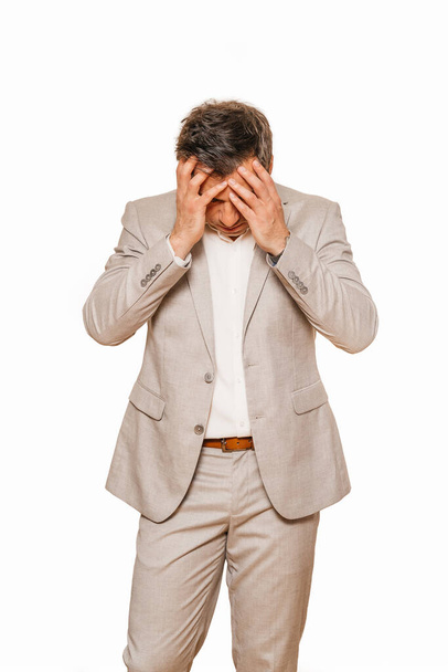 Hombre de negocios de mediana edad en suite beige, roto y deprimido como su negocio cayendo durante la recesión de coronavirus, aislado sobre fondo blanco
 - Foto, Imagen