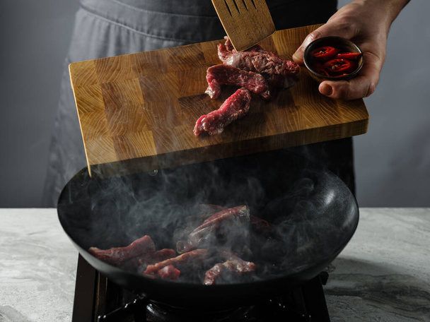 Cooking in wok pan - sliced beef meat and chilli pepper on black background, professional restaurant and hotel service food concept. - Foto, Imagen