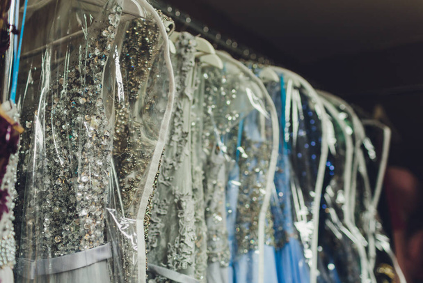 Many ladies evening gown long dresses on hanger in the dress rent shop for the wedding day. Dresses rental concept. Wedding dress for the wedding.selective focus.Ball gown rental concept. - Foto, Bild