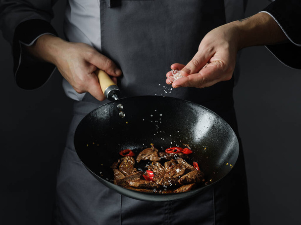Cooking in wok pan - sliced beef meat and chilli pepper on black background, professional restaurant and hotel service food concept. - Foto, imagen