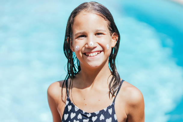 Girl looking at the camera showing the suntan lotion applied to her cheeks - Photo, Image