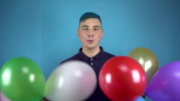 A young man with blue hair holds in his hands colorful inflatable balls. Alternative person having fun with balls on a blue background. - Materiał filmowy, wideo