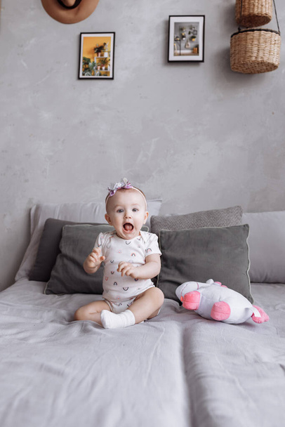 adorable little girl is playing with toy unicorn on bed at home. concept of childhood day. happy baby's, family day. - Photo, image
