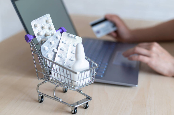 Online pharmacy concept. A woman holds a debit card in her hands and buys pills online. A girl makes an online purchase of medicines with home delivery on a laptop. - Foto, Bild