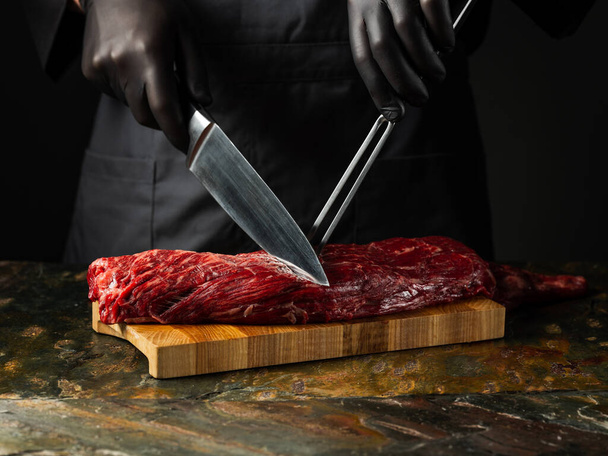 Beef fillet meat chop with big knife butcher with pepper, salt, herbs on stone table dark background. Flat top view, overview - Foto, afbeelding