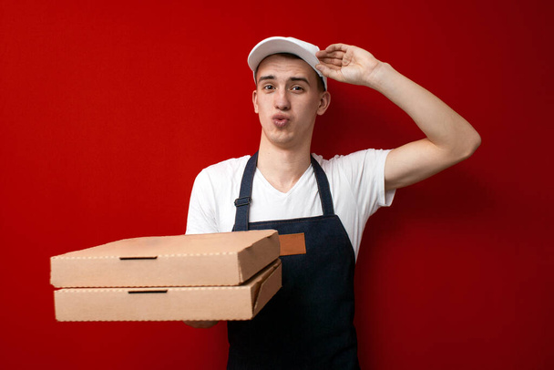 молодой удивленный доставщик пиццы дает коробки на красном фоне, шокированный курьер доставляет заказ
 - Фото, изображение