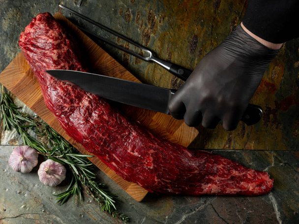 Beef fillet meat chop with big knife butcher with pepper, salt, herbs on stone table dark background. Flat top view, overview - Fotoğraf, Görsel