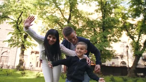 Η ευτυχισμένη οικογένεια στέκεται στο ανοιξιάτικο πάρκο και χαιρετάει με τα χέρια - Πλάνα, βίντεο