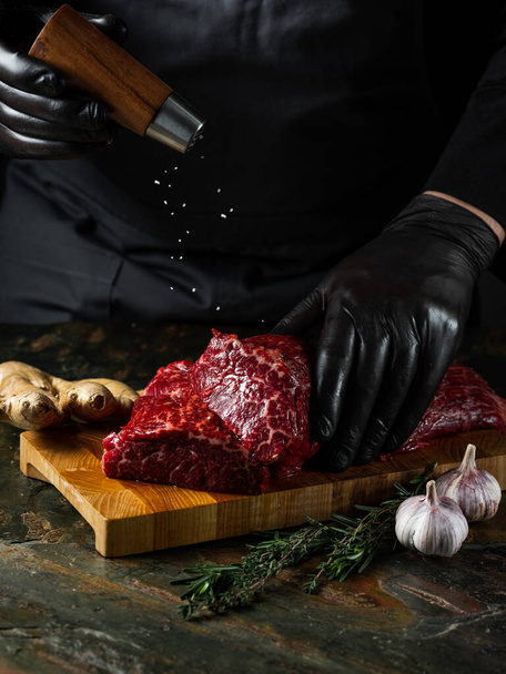 Beef fillet meat chop with big knife butcher with pepper, salt, herbs on stone table dark background. Flat top view, overview - Foto, afbeelding