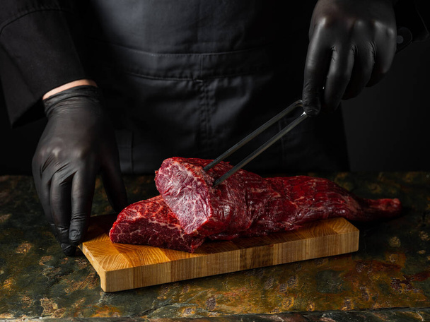 Grilled juicy beef steak selected marbled meat cutting on slices on wooden desk black background with folk and knife - Фото, изображение