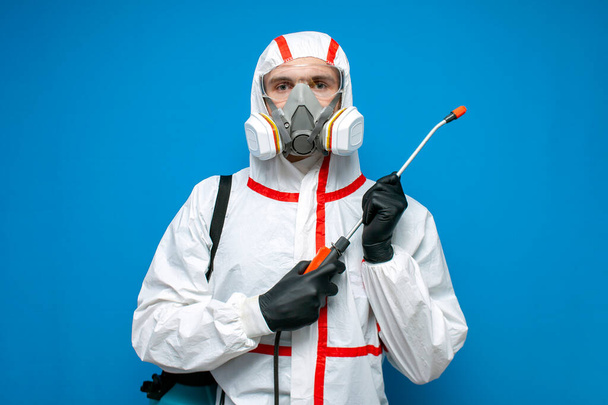 man in a chemical protective suit holds a spray bottle on a blue isolated background, epidemiologist, biologist, virologist, scientist - Photo, Image