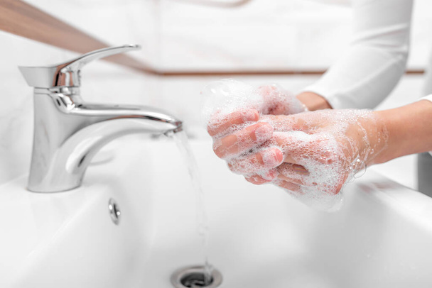 Quelqu'un se lave les mains avec du savon tout en se tenant dans la salle de bain
. - Photo, image