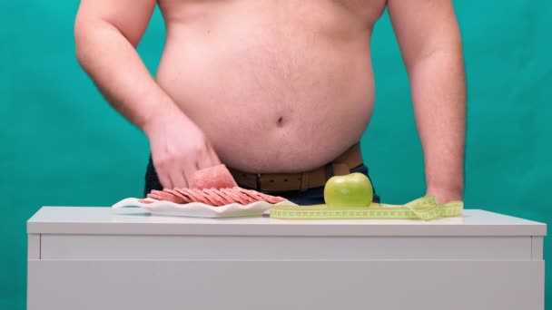 Een man met een dikke buik kiest tussen worst en een groene appel. Het concept van dieet en wilskracht. - Video
