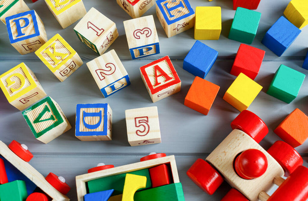 Close up Multicolored wooden cubes with letters, pencils, rainbow arc on gray background. Set of toys for studying alphabet. Education, back to school concept. Top view, copy space - Valokuva, kuva