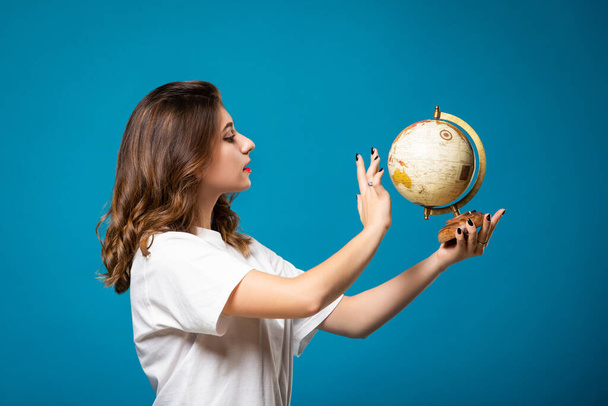 Girl points to a globe. Isolated on a blue background. Travel and tourism concept. - Valokuva, kuva