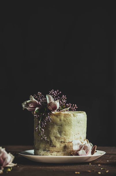 Tarta de boda blanca decorada con flores sobre mesa de madera y fondo oscuro
  - Foto, imagen