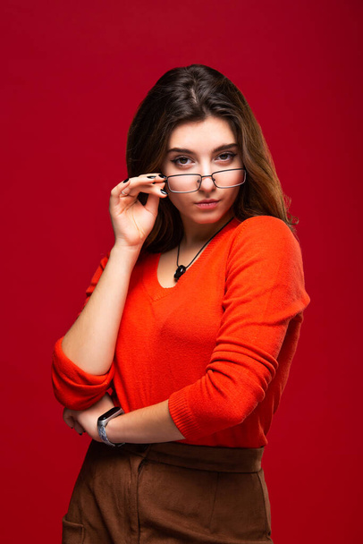 Young girl student or business woman girl in glasses with swith a pensive expression on a red background. - Photo, Image
