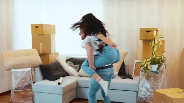 Young couple move into new apartment. Slow motion of happy positive couple spinning around. Guy hold girl on his back and dancing together. Celebrating their relocation. - Metraje, vídeo