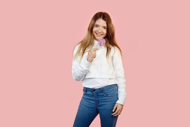 The funny girl grew up in jeans with a lollipop smiling and looking at camera - Zdjęcie, obraz