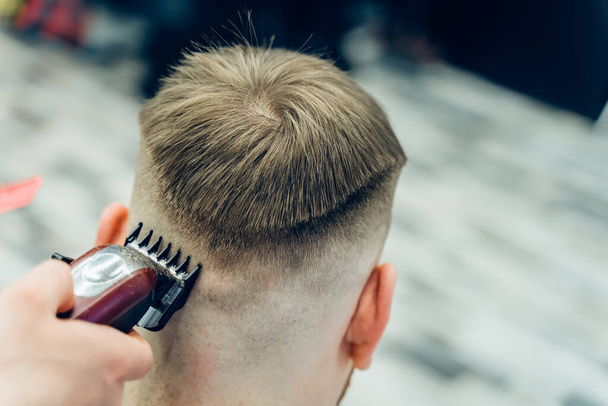 Corte de pelo masculino con afeitadora eléctrica. Peluquero hace corte de pelo para el cliente en la peluquería mediante el uso de peluquero. Peluquería hombre con afeitadora eléctrica
. - Foto, Imagen