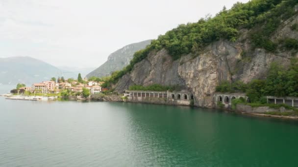 Панорамний вид на тунель Grumo в гранітній горі з високими зеленими деревами і невеликим італійським містом Lecco, озеро Комо з зеленою водою, Італія. - Кадри, відео