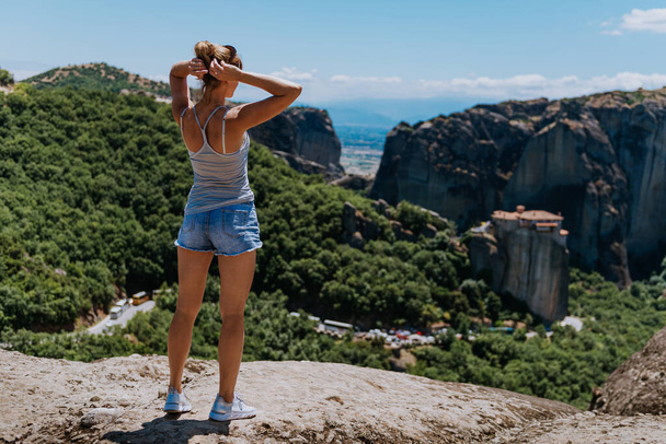 Bir kız Meteora 'nın, yani Yunanistan' ın uçurumunda duruyor ve vadiye bakıyor. yaz tatili - Fotoğraf, Görsel