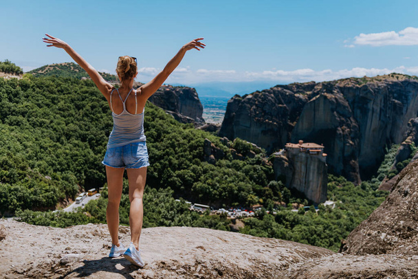 Young happy woman stands back to the camera with raised hands. Traveler enjoying the landscape with mountain, Monasteries of Meteora, Greece - Fotoğraf, Görsel