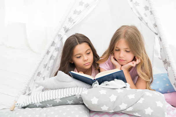 Lockdown ideas for kids. Keep studying at home. Favorite fairy tale. Book about love. Girls children lay bed read book. Pleasant time in cozy bedroom. Girls sisters cute pajamas relax and read book - Фото, изображение