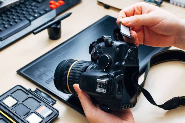 persona irreconocible sosteniendo una cámara e insertar una tarjeta de memoria en su lugar de trabajo
 - Foto, imagen
