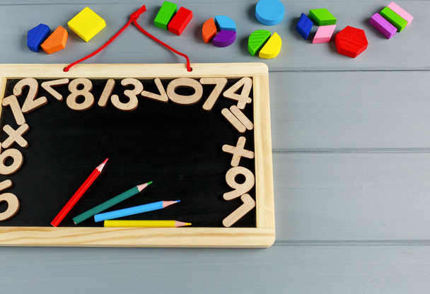 Großaufnahme einer Tafel mit Zahlen und bunten Mathefraktionen auf dem grauen Holztisch. Interessante Mathematik für Kinder im Hintergrund. Bildung, zurück zum Schulkonzept - Foto, Bild
