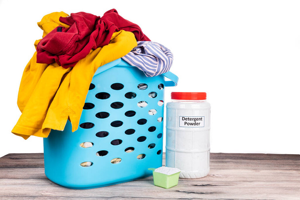 Détergent à lessive en poudre à côté du panier plein de vêtements sur une surface en bois sur fond blanc
 - Photo, image