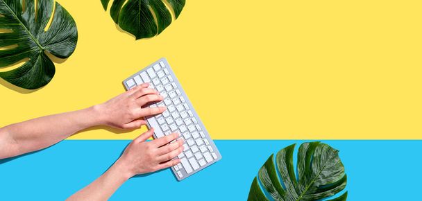 Person using a computer keyboard with tropical leaves - Photo, image