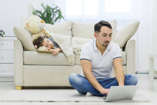 Tata jest online, podczas gdy jego córka śni na kanapie. - Zdjęcie, obraz
