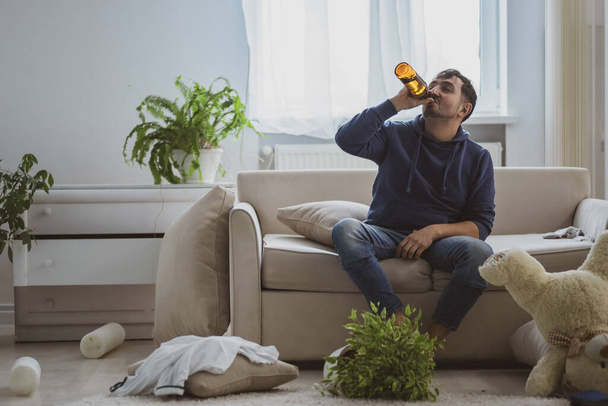 Handsome depressed man drinking alcohol at home. - Фото, изображение