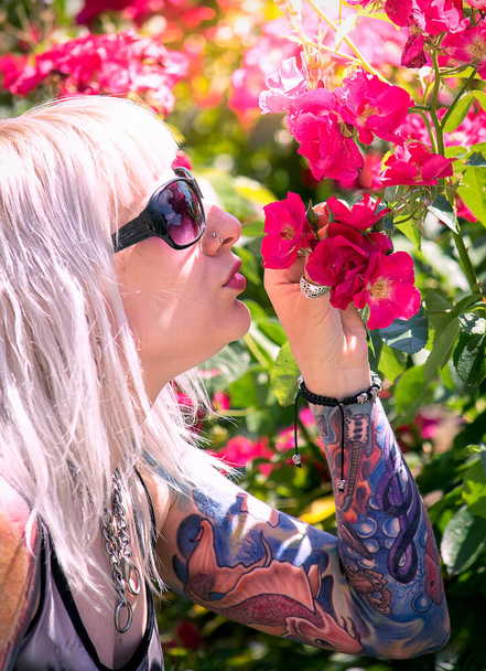 Kobieta z tatuażem z pełnym rękawem wąchająca kwiaty - Zdjęcie, obraz