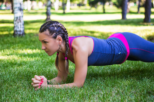 athletische Frau bei einer Übung an der Presse, Planke steht auf seinen Ellbogen. Im Park auf dem Rasen. - Foto, Bild