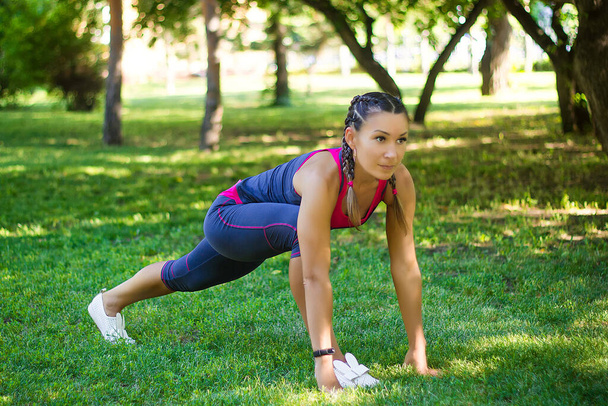 Sports woman doing exercises for stretching the legs, sits on the splits. In the park on the lawn. - Photo, image