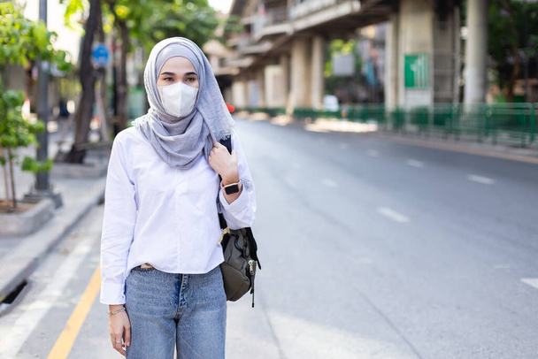 Donna musulmana asiatica che indossa una maschera medica per prevenire la polvere e l'infezione del virus in piedi lungo la strada in città. Concetto di Coronavirus (covid-19)
. - Foto, immagini