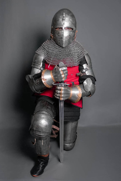 A young knight in medieval armor with a weapon in his hands kneeled. - Valokuva, kuva