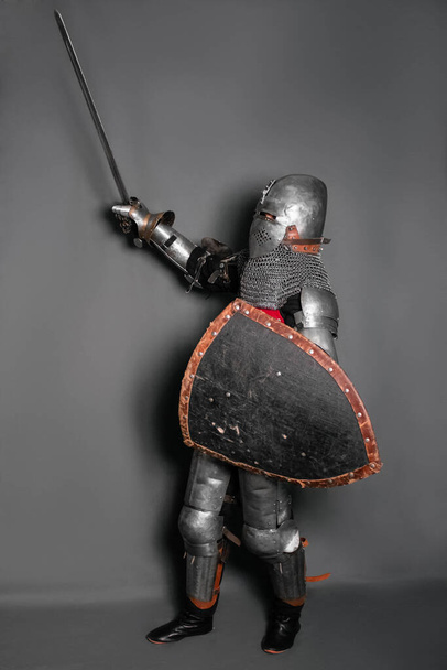 A medieval knight in armor with a shield and a sword in his hands stands in a fighting position and waves his weapon. - Foto, immagini