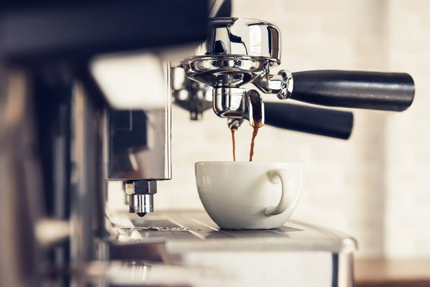 Koffie die wordt gebrouwen door de machine stroomt door portafilter in de beker in cafe - Foto, afbeelding