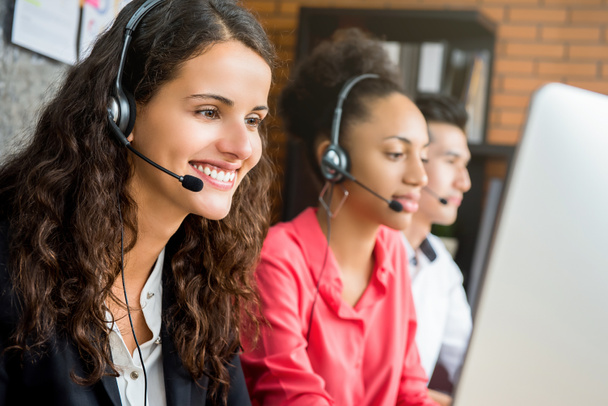 Sorrindo bela mulher de negócios trabalhando em call center como uma operadora de telemarketing com sua equipe internacional
 - Foto, Imagem