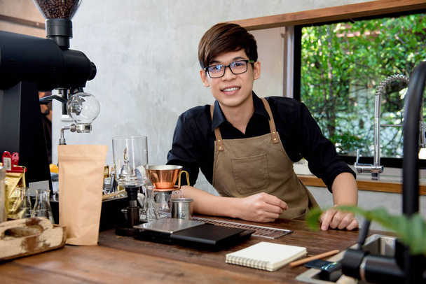 Young Asian entrepreneur sitting at counter in his own coffee shop - Photo, Image