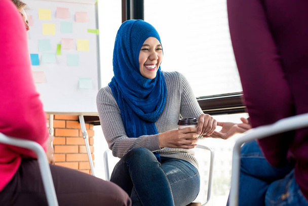 Νεαρή μουσουλμάνα γυναίκα που μιλάει και γελάει με τους φίλους της χαρούμενα στην ομαδική συνάντηση - Φωτογραφία, εικόνα